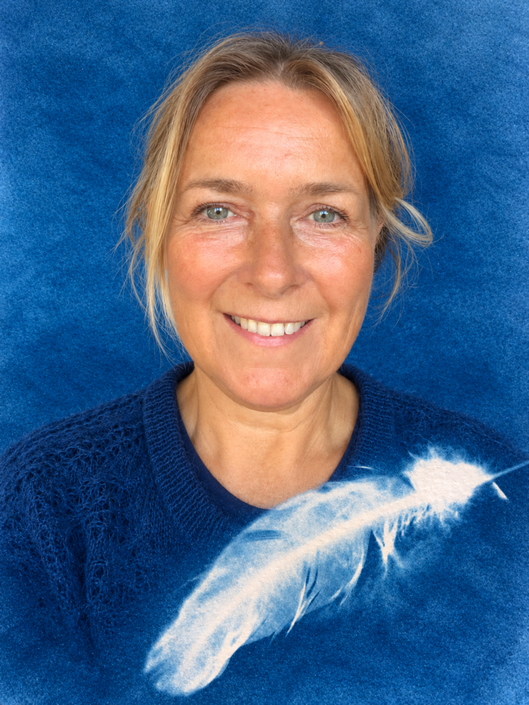 Joyce van Blauwe Zon Kunstlab met een blauwe cyanotypeachtergrond en wit veertje